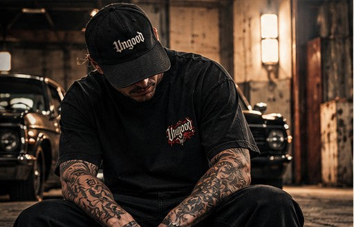 Tätowierter Mann mit Ungood-Cap und -Shirt in einer Werkstatt